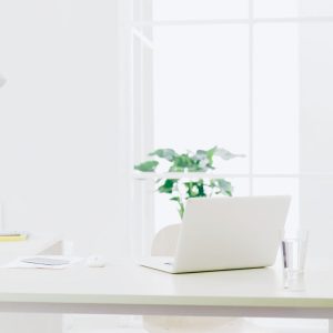 Heller Arbeitsplatz mit Laptop am Fenster als Symbol dafür, Sinn im Job zu finden und Arbeitszeit bewusst als Lebenszeit zu erleben