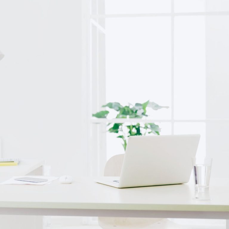Heller Arbeitsplatz mit Laptop am Fenster als Symbol dafür, Sinn im Job zu finden und Arbeitszeit bewusst als Lebenszeit zu erleben